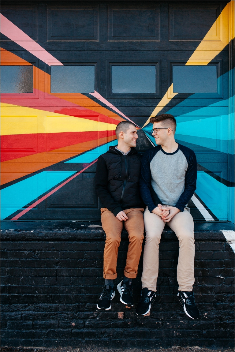 Two men sitting next to each other smiling RiNo Denver engagement photos