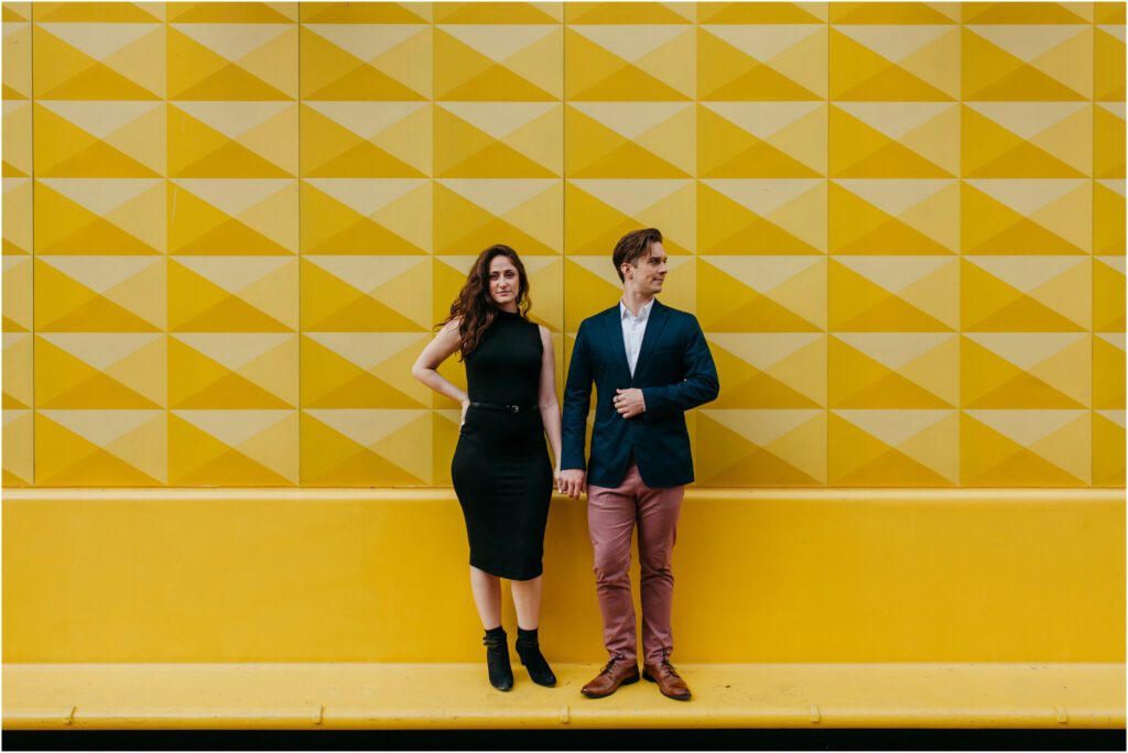 Couple holds hands standing on yellow bench in city